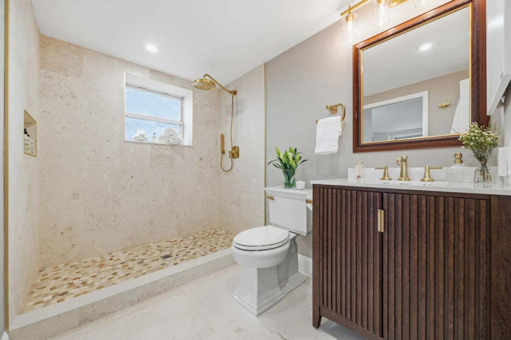 Bathroom remodeled with pebble-tile shower floor, gold fixtures, and dark wood vanity by Keen Improvements