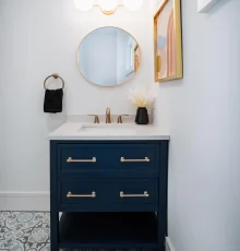 Navy blue bathroom vanity with white countertop, round mirror, and patterned tile floor remodeled by Keen Improvements in Hudson Valley.